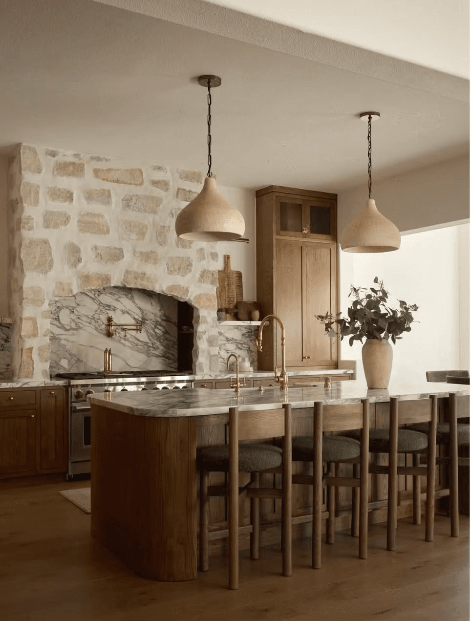 Custom wood kitchen cabinetry with marble island and stone range alcove
